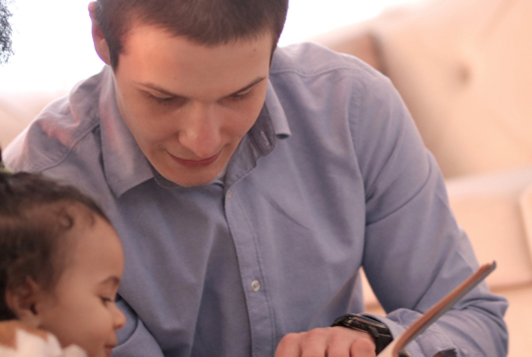 Close up of a man in a blue shirt reading to a small child.