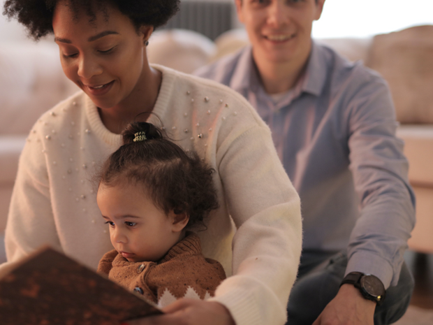 Two adults sitting on the floor with a young child. The child is sitting on the woman's lap.