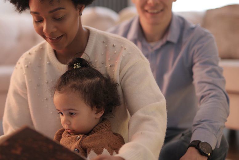 Two adults sitting on the floor with a young child. The child is sitting on the woman's lap.