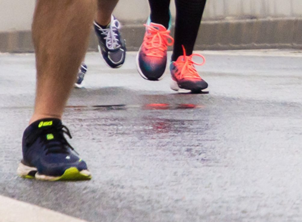 Runners’ feet in motion during a road race, representing a community fundraising run or charity event.