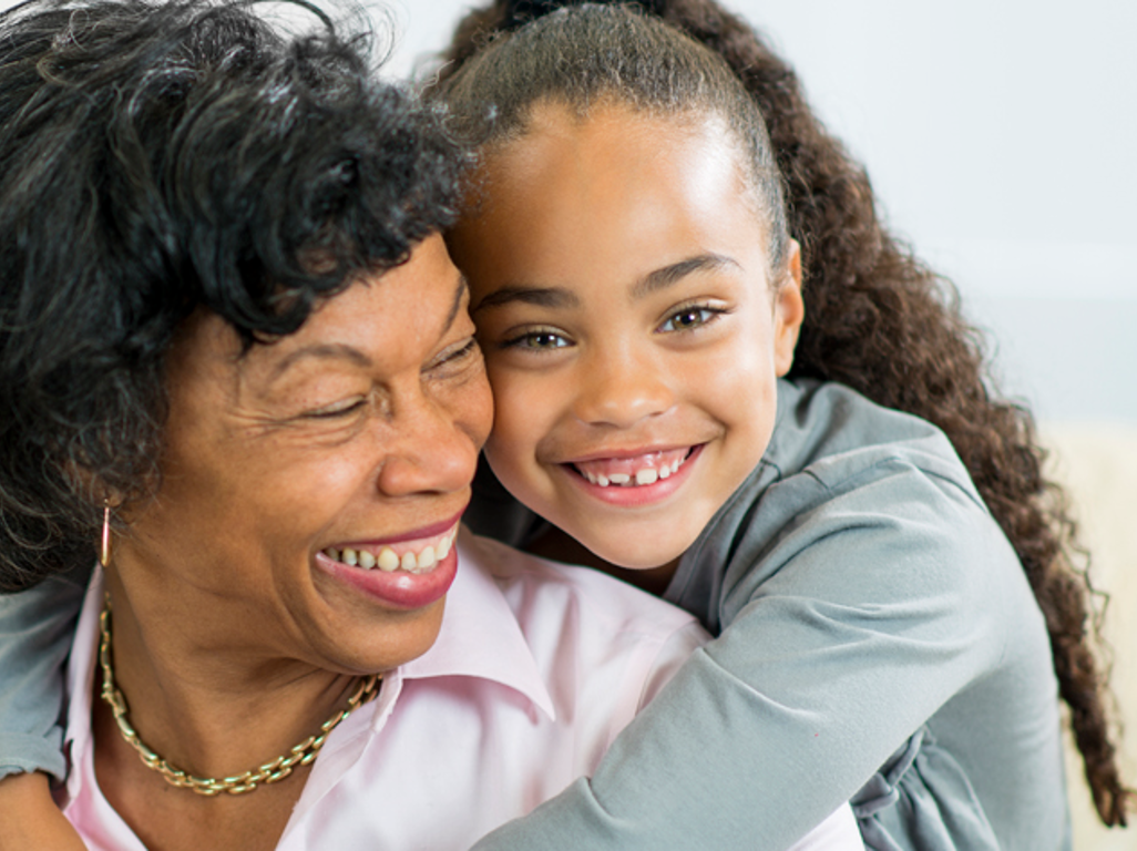 Older woman smiling while a young child embraces her, she is also smiling 