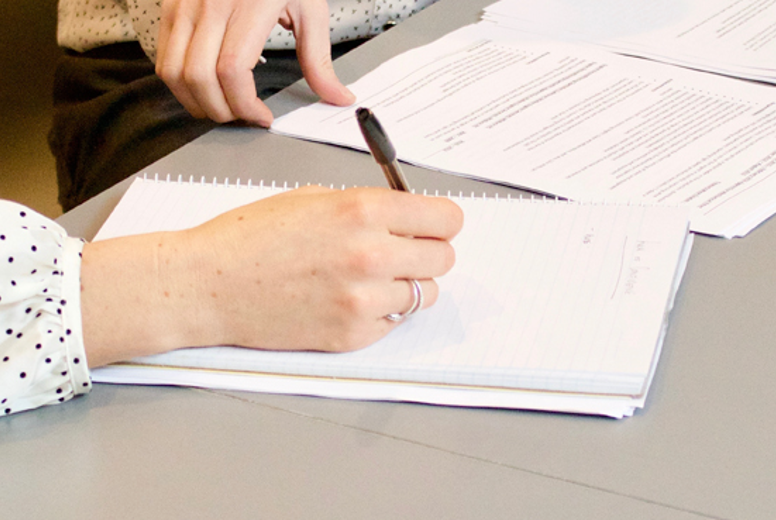 A close up of a notebook on a table. Someone is writing on the paper with a pen.